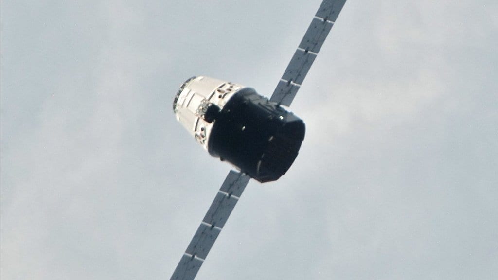 A Dragon cargo capsule with extended solar arrays, seen at close range from the International Space Station.