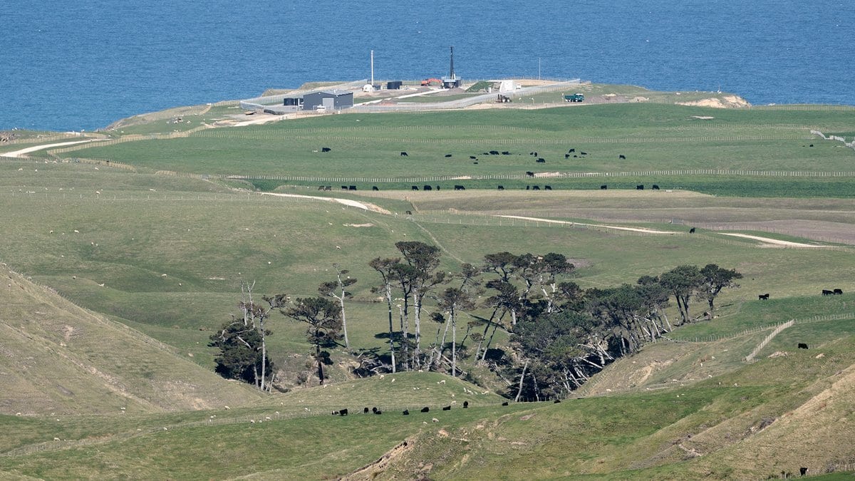 A green coastal headland above the sea, with the low buildings and launch tower of Rocket Lab's Launch Complex 1 standing on the point.