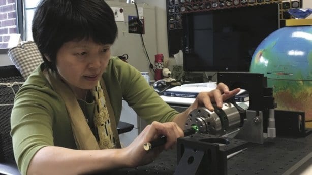 A researcher aligns a green laser into a diamond anvil cell mounted on an optical bench.