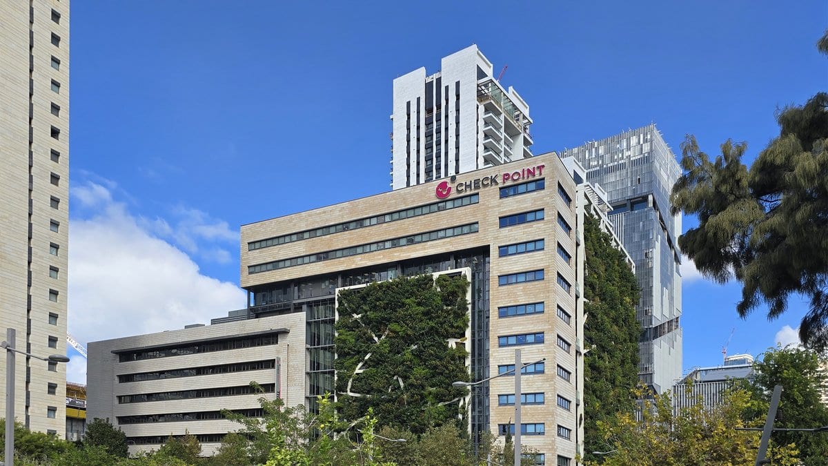 A stone and glass office tower in Tel Aviv with a Check Point logo sign along its roofline, seen from a park on a clear day.