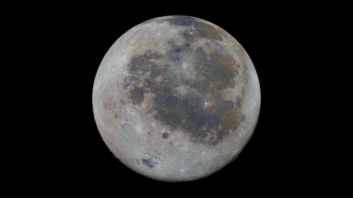 The full Moon against a black sky, gray highlands and darker maria spread across the disk, with faint color differences over the surface.