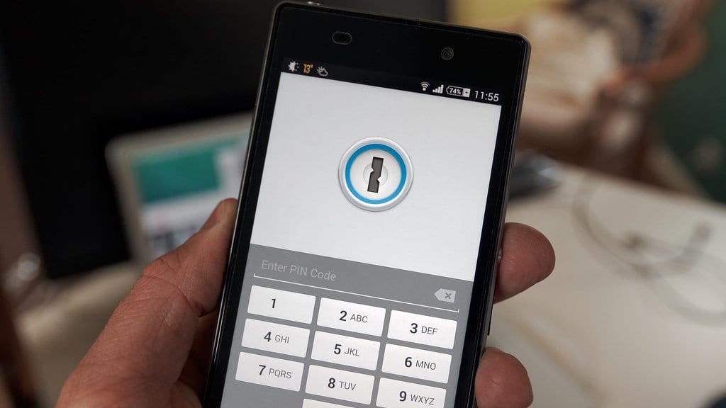 A hand holds an Android phone showing a password manager app locked behind a PIN keypad.