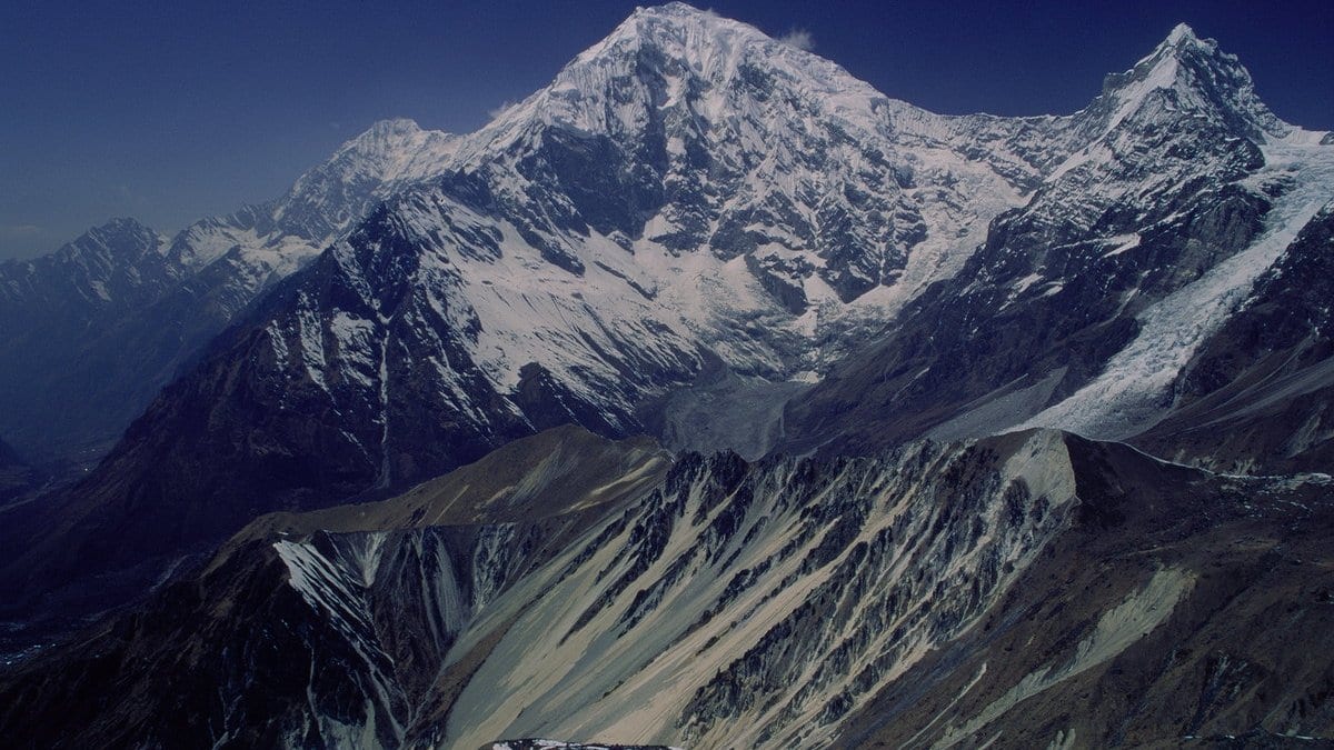Snow and ice on the steep face of Langtang Lirung in Nepal, with a debris-covered glacier and moraine ridges in the valley below