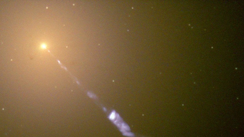 A bright galactic nucleus at upper left with a narrow blue jet of glowing knots streaming diagonally away from it.