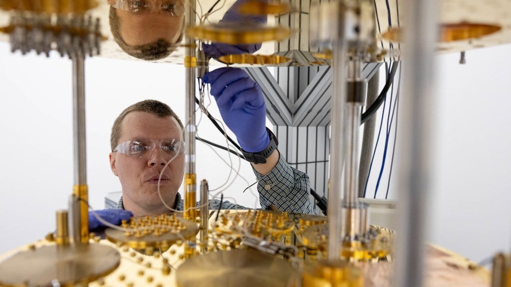 A researcher reaches between the gold-plated cooling stages of a dilution refrigerator to connect wiring inside the cryostat.