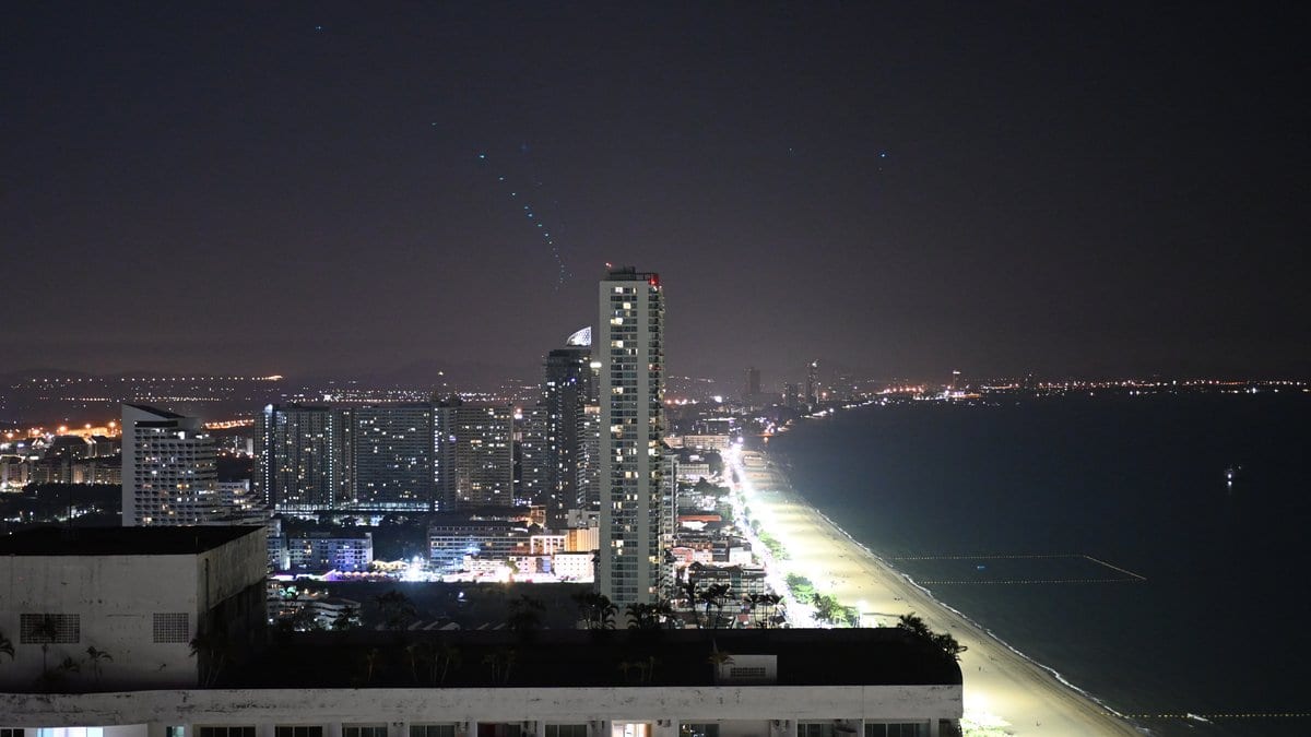 A coastal city at night seen from above, with a brightly lit beachfront strip running along a dark bay.