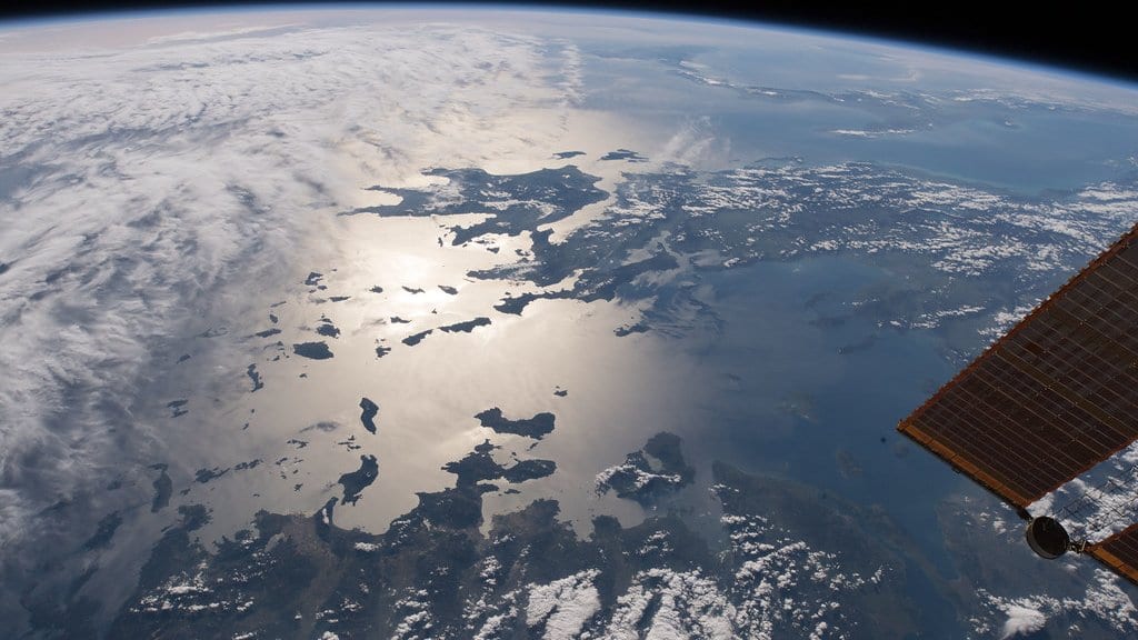 Sunlight glints off the Aegean and Ionian Seas around the Greek islands, photographed from the International Space Station, with a station solar array at the right of the frame.