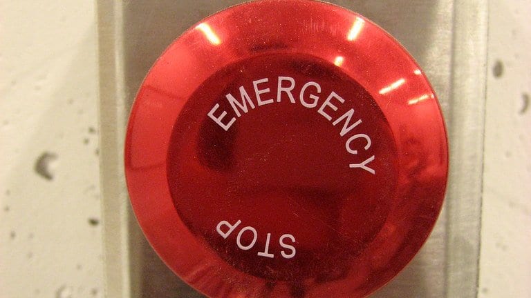 A round red button labeled Emergency Stop, mounted in a brushed stainless steel wall plate.