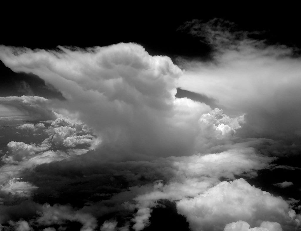 A tall cumulonimbus cloud with a flattened anvil top, seen from above the surrounding cloud deck
