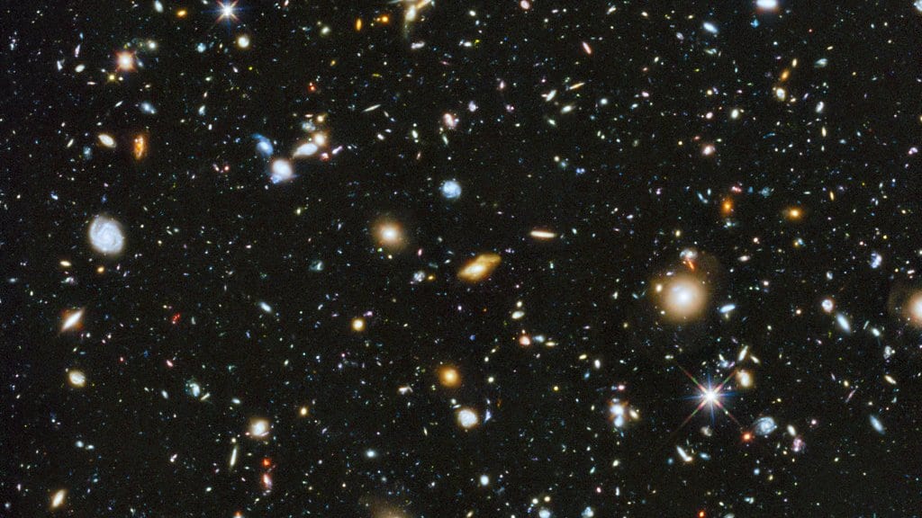 A small patch of sky crowded with thousands of galaxies of many shapes and colors against black space, the Hubble Ultra Deep Field.