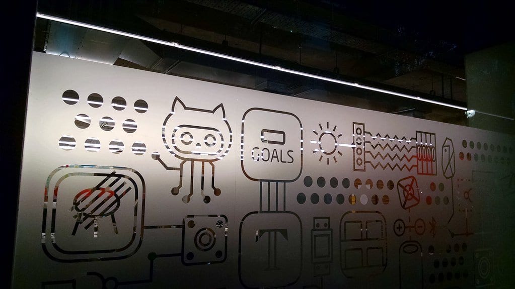 A backlit glass panel etched with GitHub's Octocat mascot and rows of small technical icons, seen inside a building at night.
