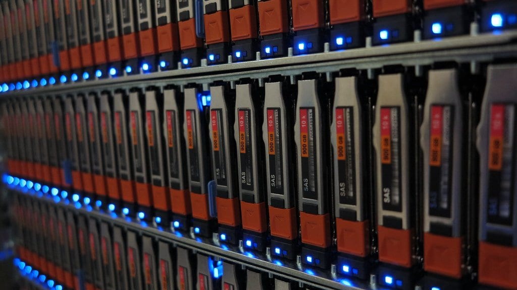Close-up of rows of hot-swap disk drives in an enterprise storage array, with blue activity lights along each row.