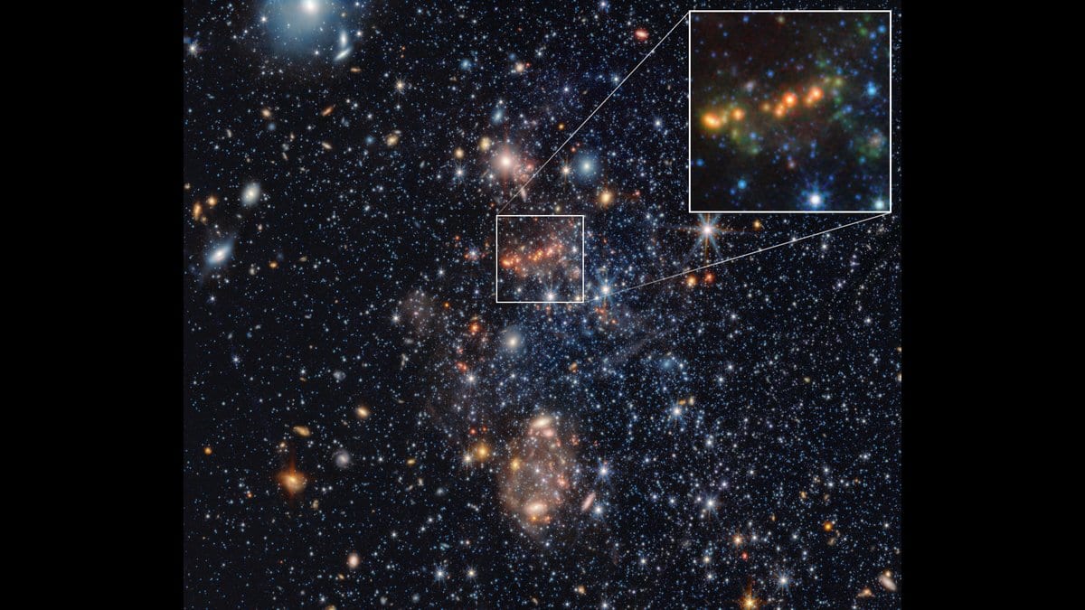 Infrared view of the dwarf galaxy Sextans A, a loose spread of blue and orange stars on a dark sky, with a white box marking a small region that is enlarged at upper right to show a chain of orange and green knots.