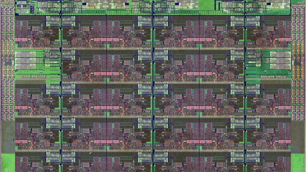 Extreme close-up photograph of the silicon die of an Intel Skylake-SP Xeon server processor, showing a regular grid of repeating circuit blocks in green and pink.