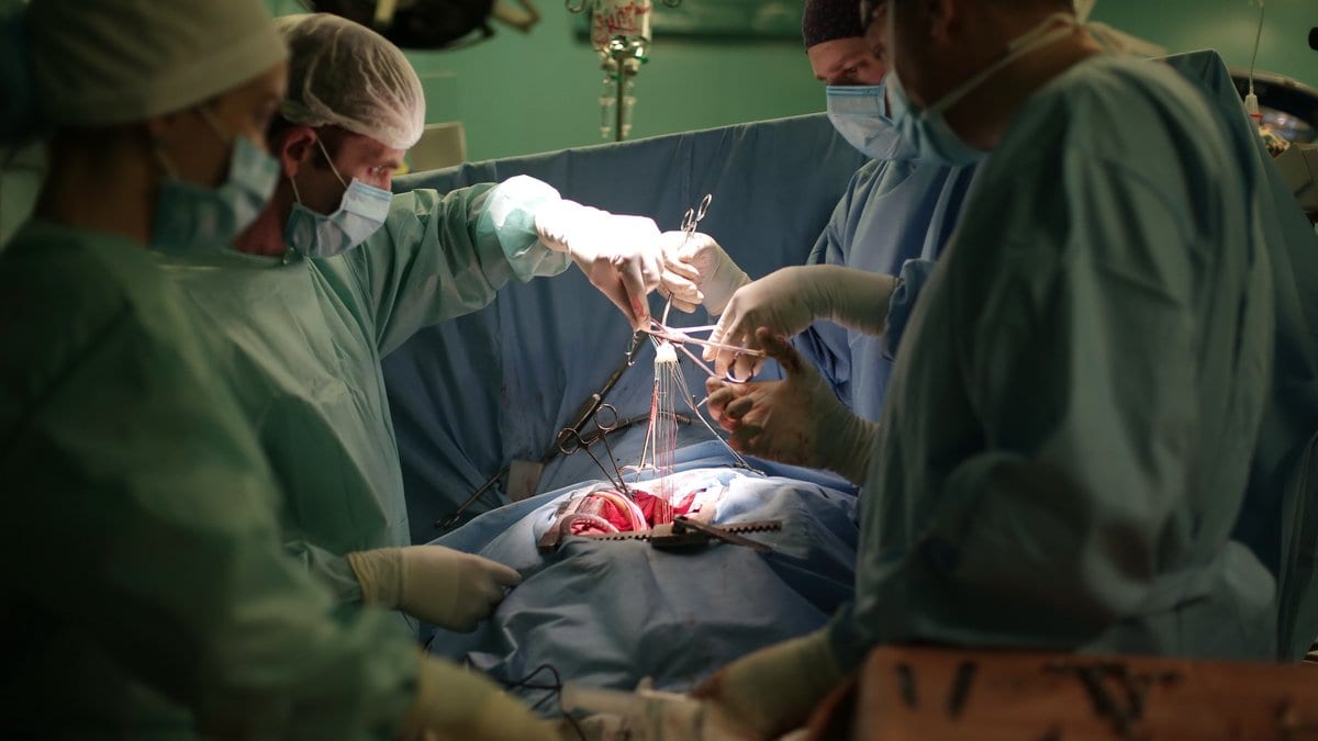 A surgical team in gowns and masks works over an open chest during a heart operation.