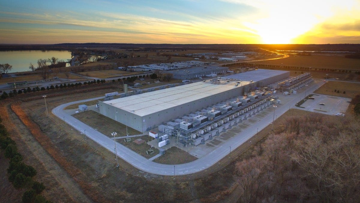 Aerial view at sunset of a long Google data center building with rows of rooftop cooling units, beside farmland and a river.