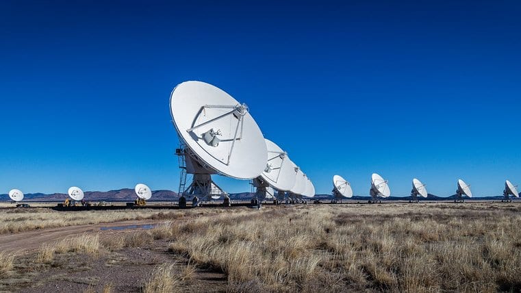 A line of white dish antennas stretches across a grassland plain in New Mexico under a deep blue sky.