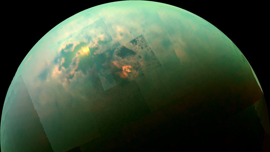 Titan's northern hemisphere in near-infrared, with dark lake basins visible through the moon's hazy atmosphere.