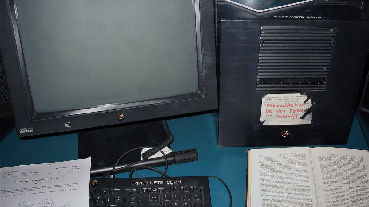 An early black NeXT desktop computer and its monitor on display, with a handwritten paper note taped to the machine saying that it is a server and must not be powered down.