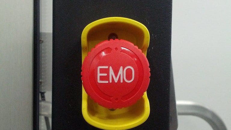 A red emergency machine off button labeled EMO, set in a yellow guard on a black box mounted to metal equipment framing.