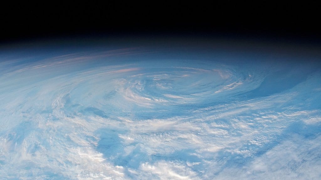 A wide spiral of cloud over the South Pacific Ocean photographed from orbit, with the dark edge of space above the horizon.