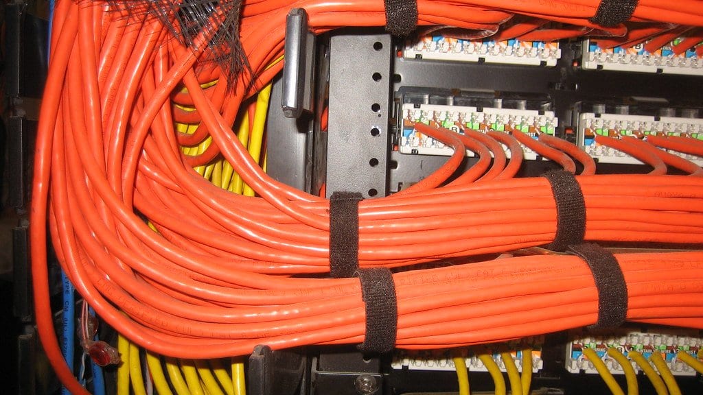 Bundles of orange and yellow network cables plugged into the rear of a rack mounted patch panel.