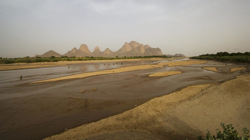A braided river channel reduced to shallow threads of water between wide sand bars, with mountains on the horizon.