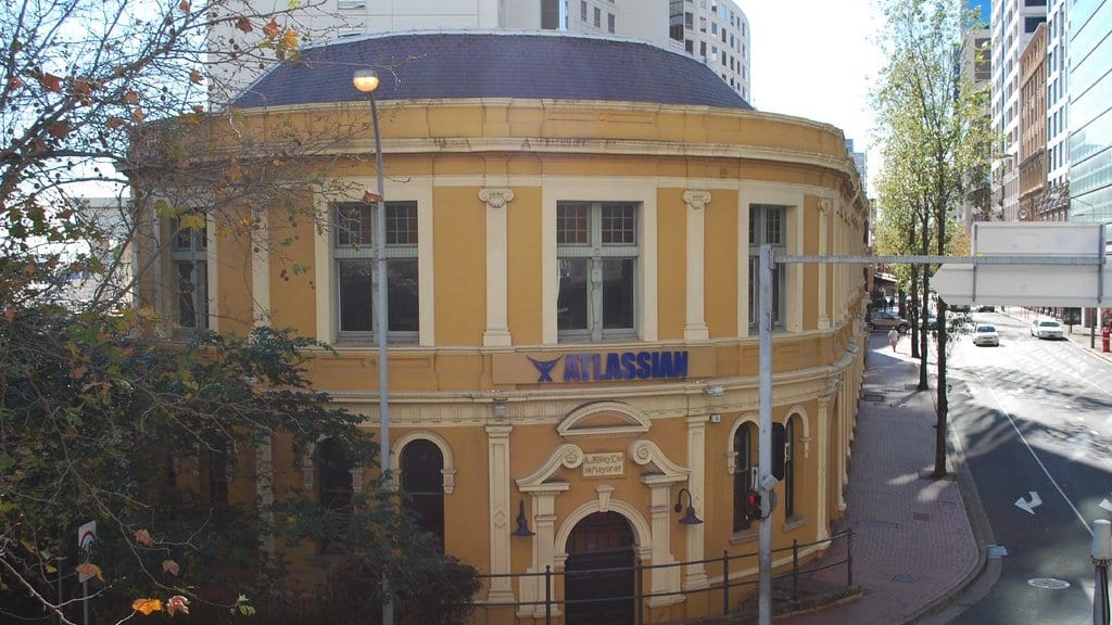 A yellow heritage corner building on a city street with a blue ATLASSIAN sign across its facade.