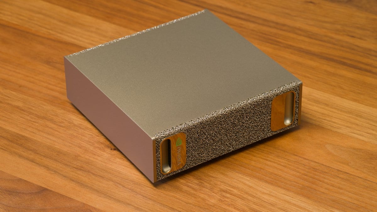 A small silver desktop computer, the NVIDIA DGX Spark, on a wooden desk, with a front panel of coarse metal foam.