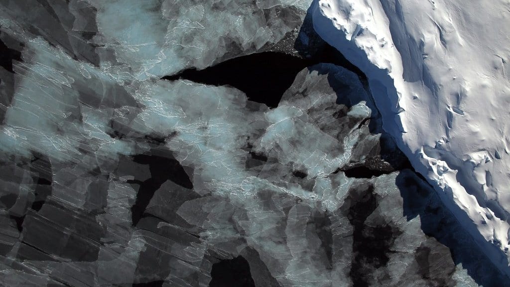 Fractured sea ice floes separated by dark open water beside a smooth ice edge, seen from above in the Bellingshausen Sea off West Antarctica.