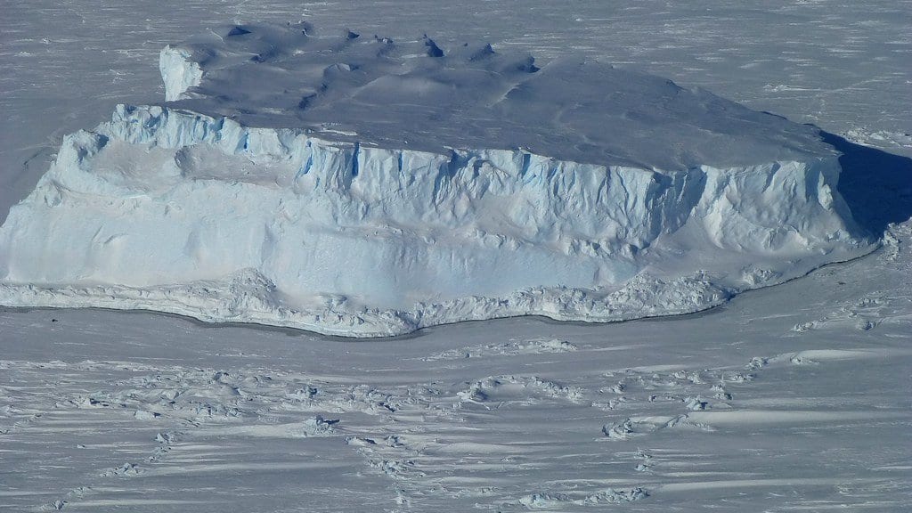 An aerial view of a flat-topped iceberg held fast in the surrounding Antarctic sea ice.
