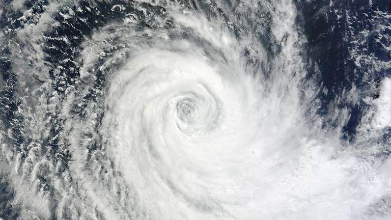 A tropical cyclone photographed from orbit, a small eye at the center of a tight white spiral of cloud over dark ocean.