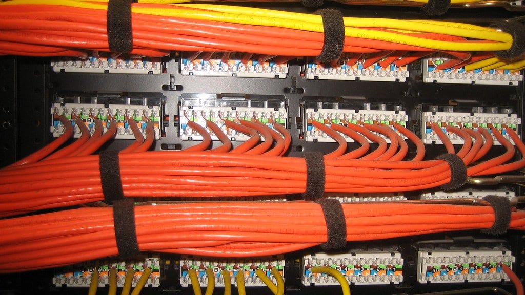 Bundles of orange and yellow network cables terminated into the back of a rack-mounted patch panel.