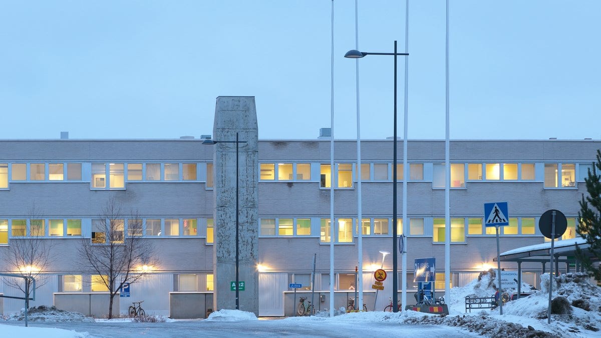 The lit facade of a hospital in Oulu, Finland, on a winter evening, with snow banked along the road in front of it.