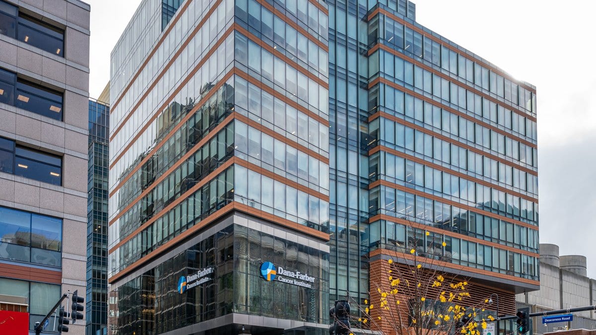 A glass and brick cancer treatment center on a Boston street corner, with signage for the Dana-Farber Cancer Institute above its ground-floor entrance.