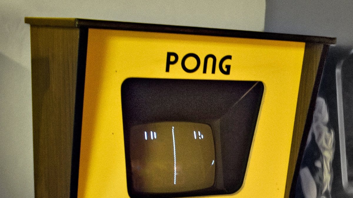 A yellow Atari Pong arcade cabinet, the game name in black lettering above a small screen showing two paddles and a center line.