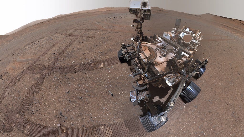 A self-portrait of NASA's Perseverance rover on the Martian surface, with its own wheel tracks crossing the dusty ground around it.