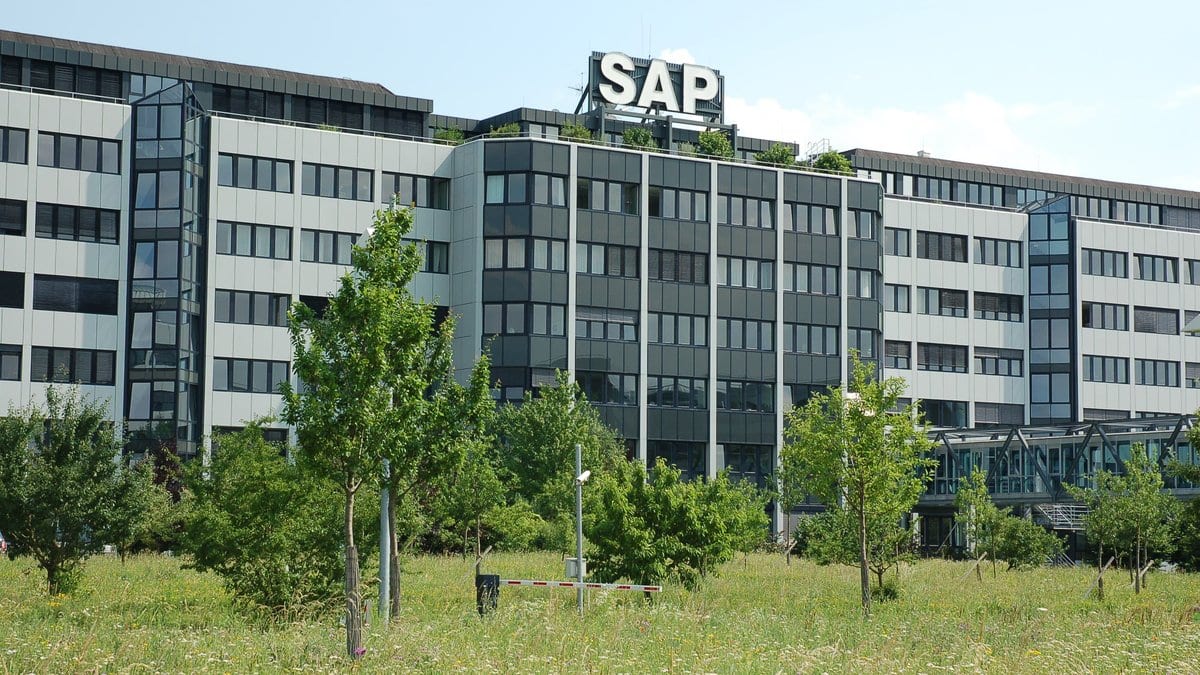 An office complex with a large rooftop sign reading SAP, seen across a grassy field under a clear sky.