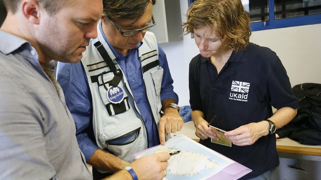 Three humanitarian experts examine a printed map of Dominica, one of them marking it with a pen.