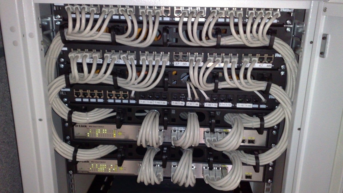 An open equipment cabinet holding patch panels, two rack-mounted Ethernet switches and a router, wired with looped gray network cables.