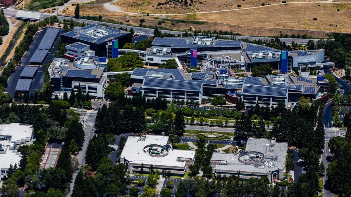 Aerial photograph of Google's headquarters complex in Mountain View, California, with low office buildings, solar panels on the roofs and landscaped grounds.