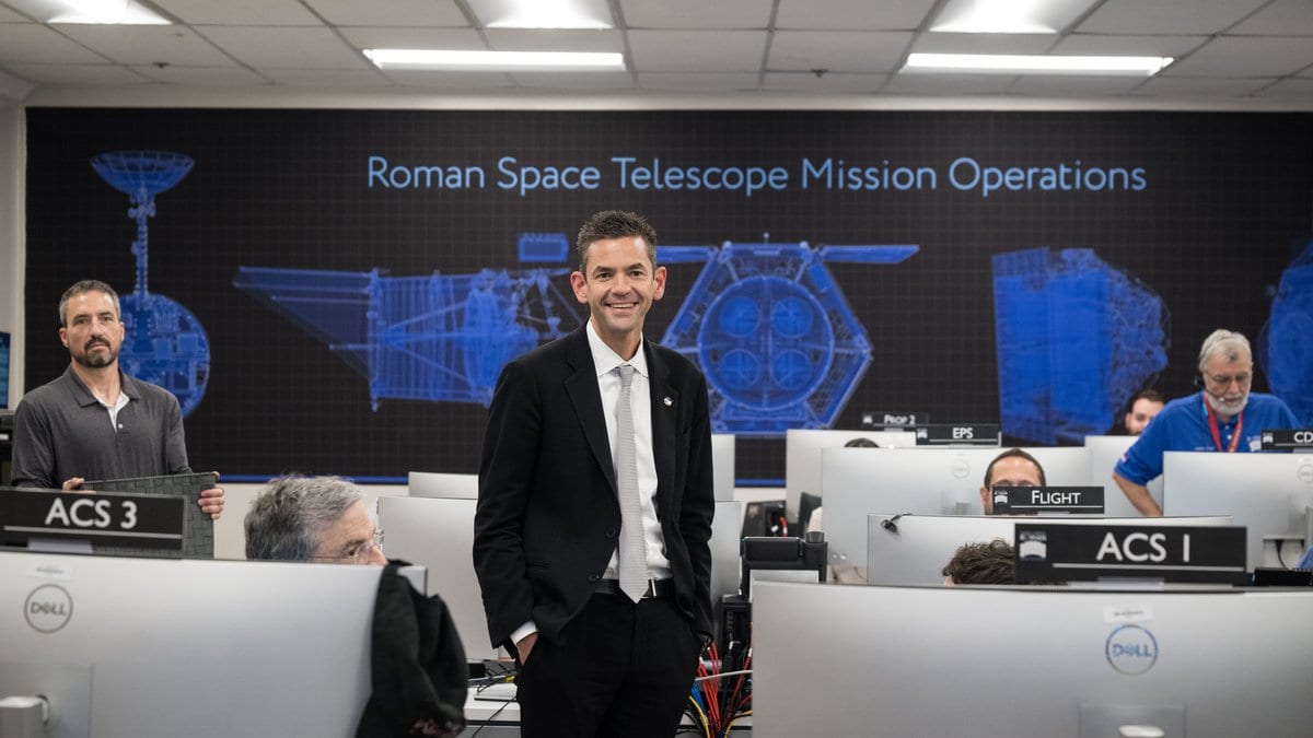 A mission operations room whose back wall carries a large blue graphic labeled Roman Space Telescope Mission Operations, with engineering drawings of the spacecraft.