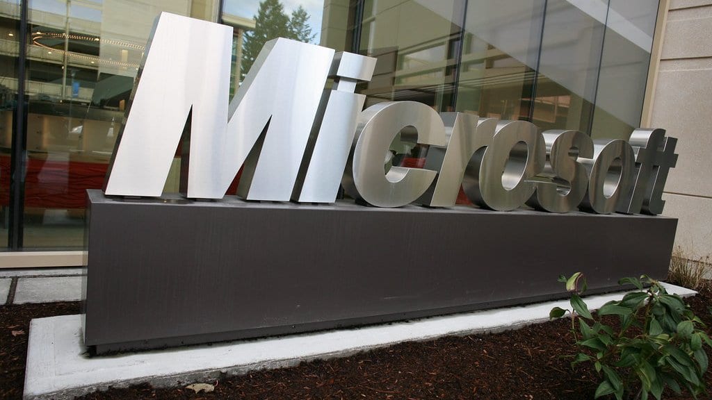 Freestanding brushed metal Microsoft lettering on a low plinth in front of a glass office facade.
