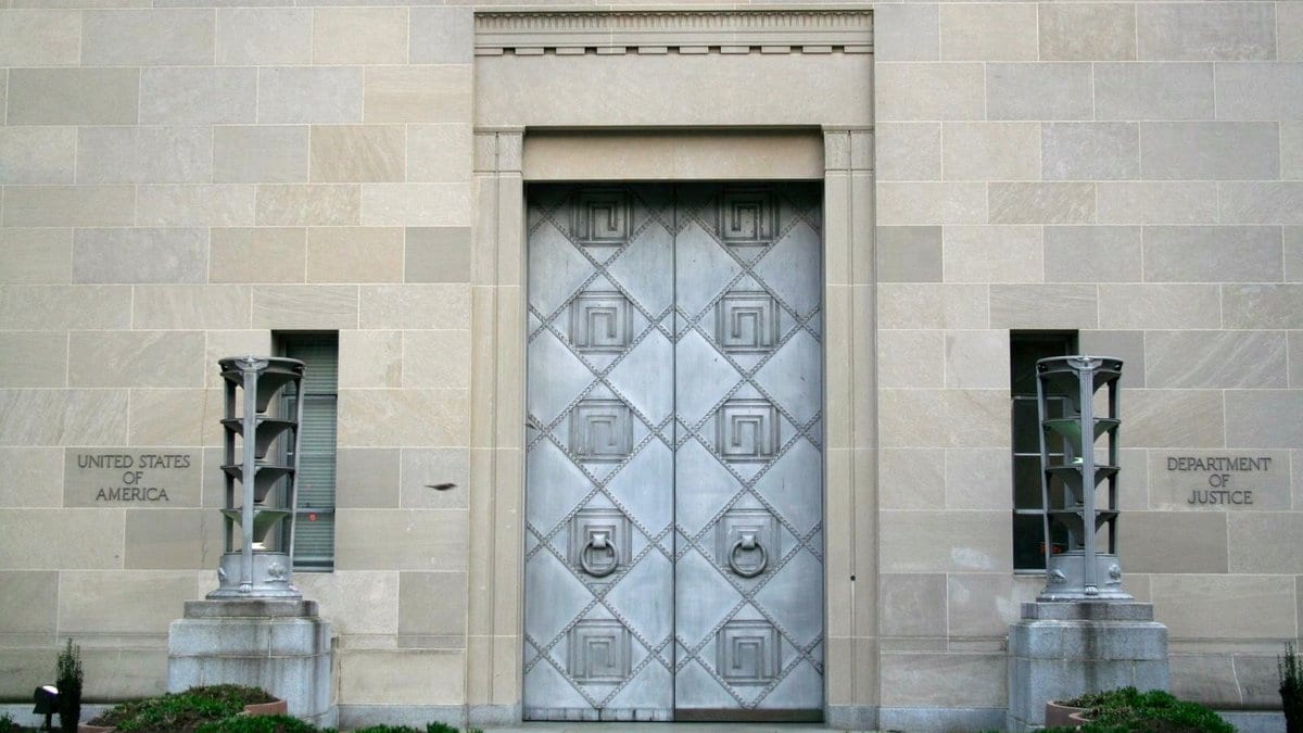 Tall metal doors set into the stone wall of a federal building in Washington, with the words United States of America carved into the stone at left and Department of Justice carved at right.