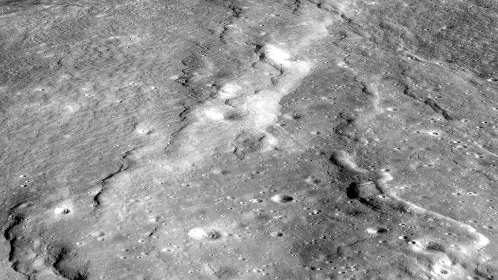 An oblique view of the lunar surface in which a long, low cliff winds across a cratered plain, its face thrown into shadow by a low sun.