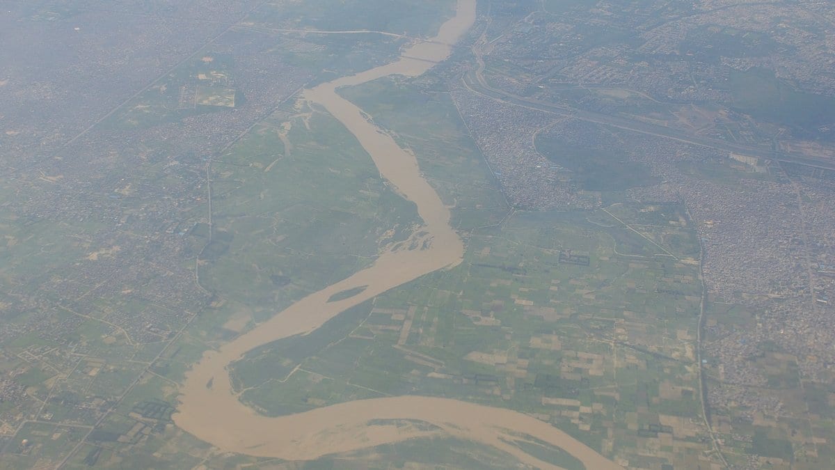 Aerial photograph of a silt-brown river meandering across green farmland, with a dense city spreading along one bank.