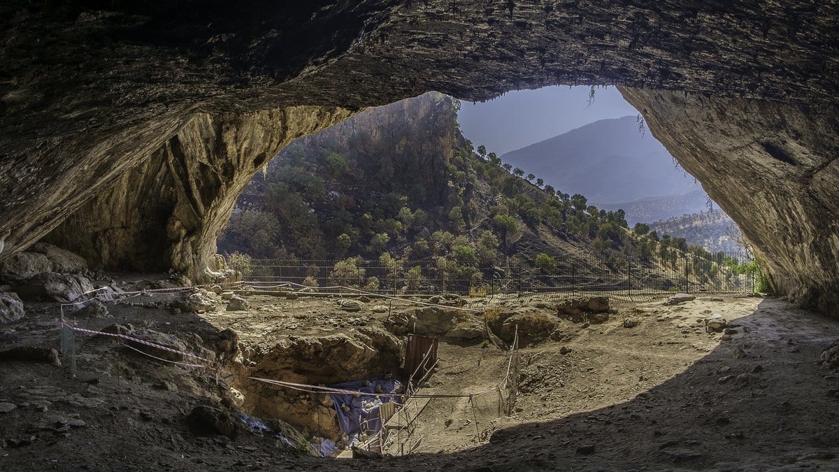 The interior of Shanidar Cave in Iraqi Kurdistan, with daylight at the cave mouth and fenced excavation areas on the cave floor.