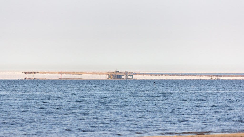 A calm sea under a pale sky, with a distant shoreline stretched into a flat band that appears to float above the horizon.