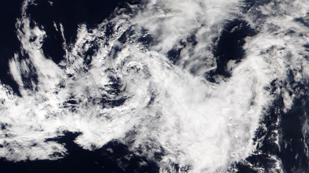 Satellite view of a loosely organized spiral of white cloud over dark open ocean water, with no land visible
