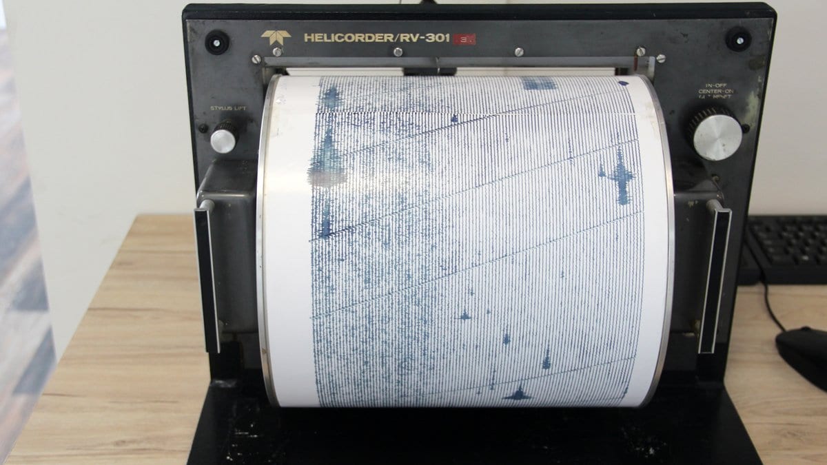 A paper drum recorder with a dense seismogram trace wrapped around its rotating drum.